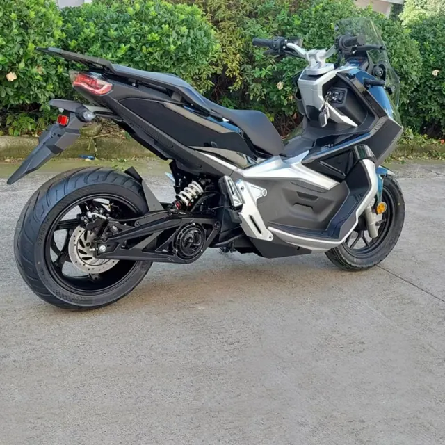 Scooter électrique noir vu de trois-quarts arrière, avec le feu arrière, la roue arrière et son disque de frein, sur un sol bétonné devant une haie.